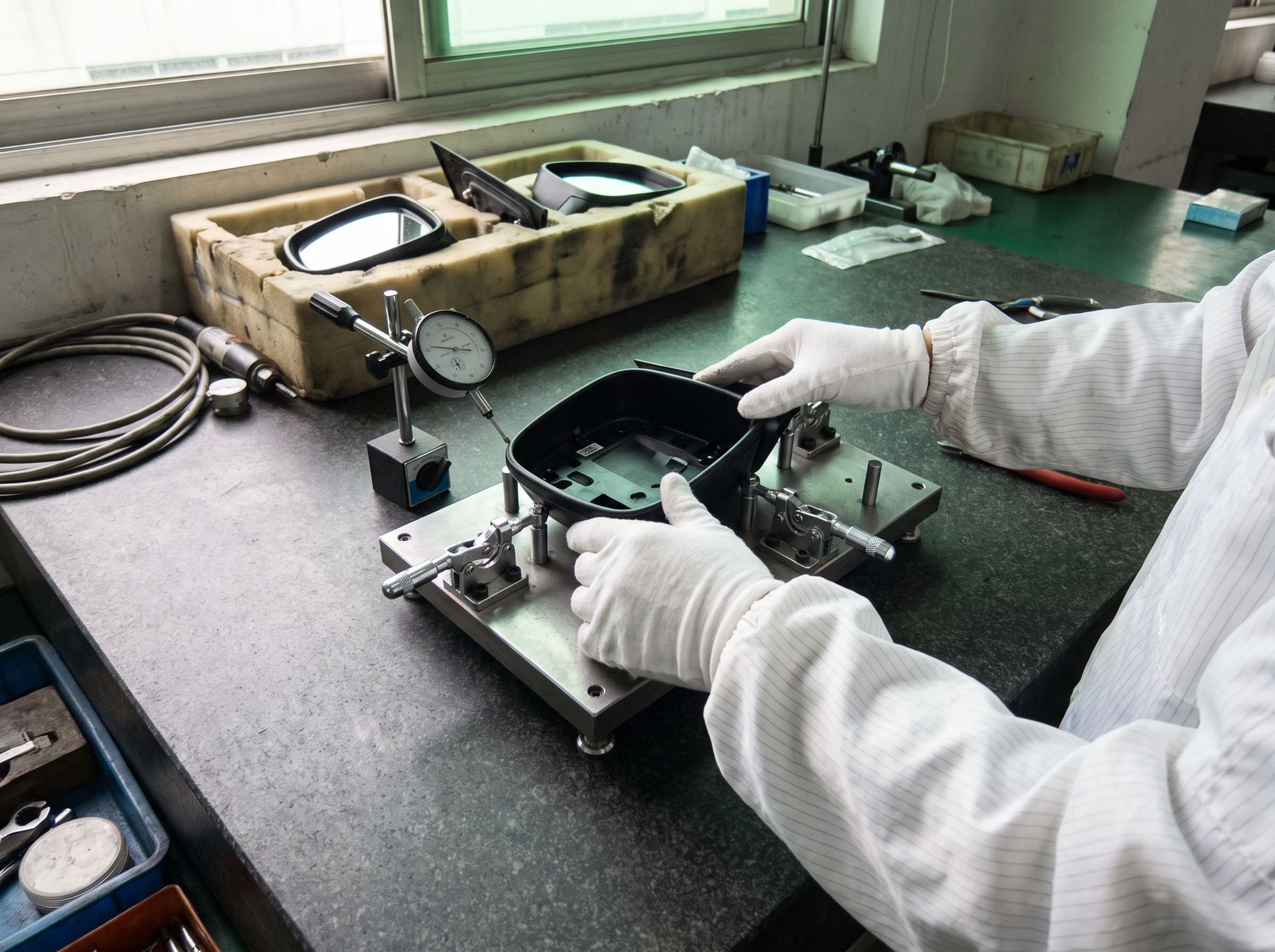 White-gloved hands placing a mirror housing on a checking fixture, dial indicator in contact