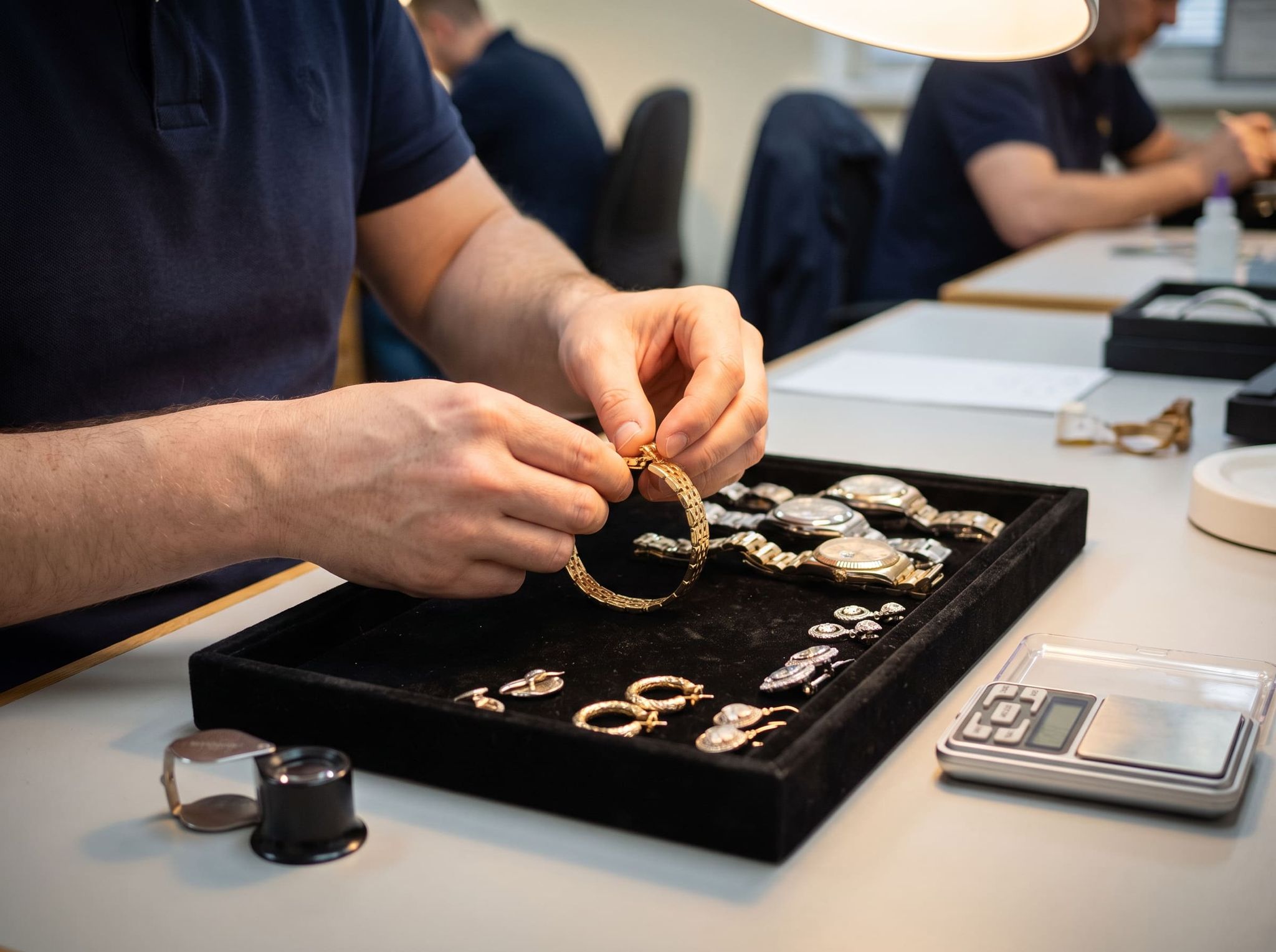 Checking the clasp of a bracelet above a tray of watches and jewelry