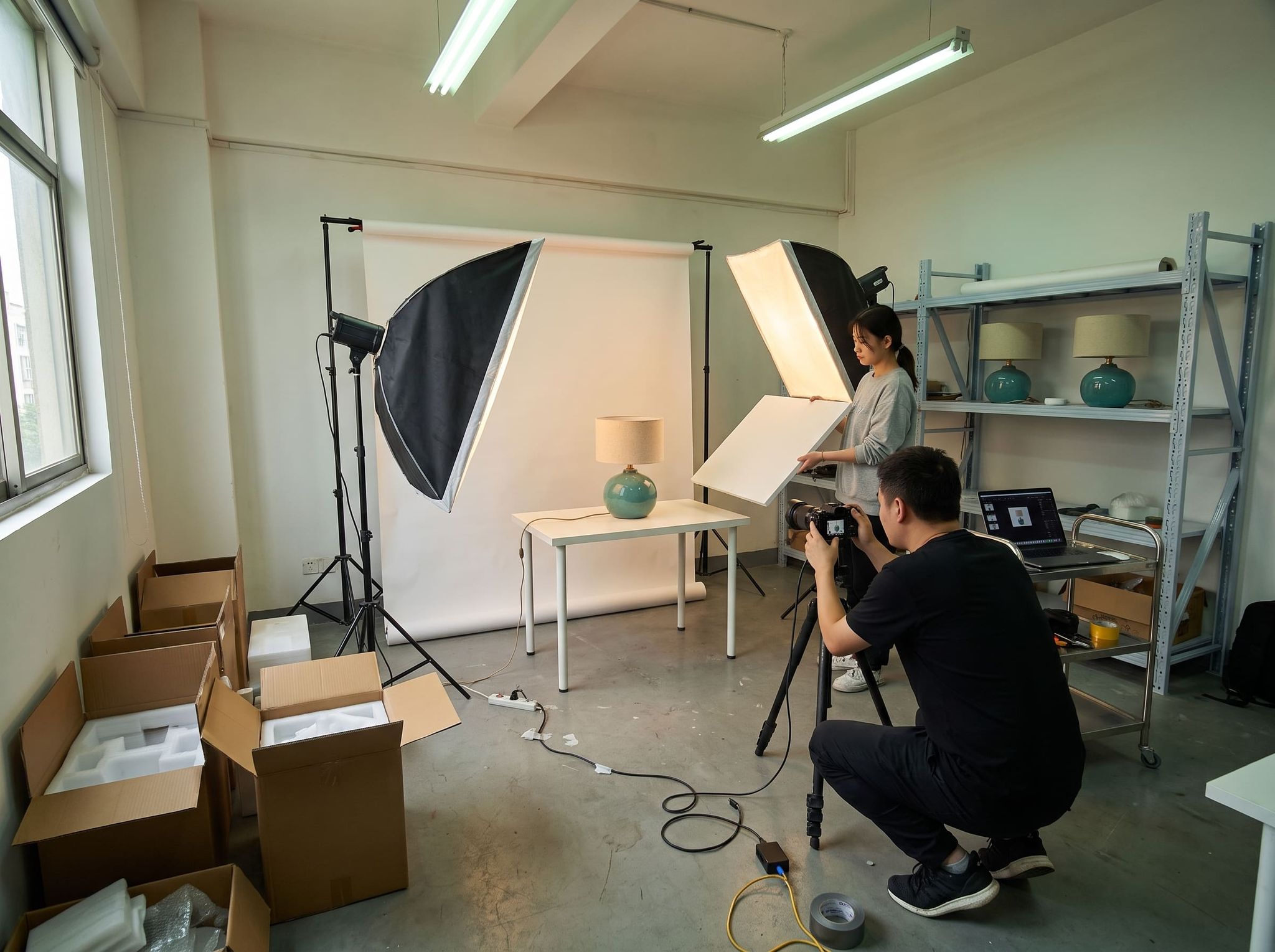Photo shoot of a ceramic lamp in a photo studio, an assistant adjusting a reflector